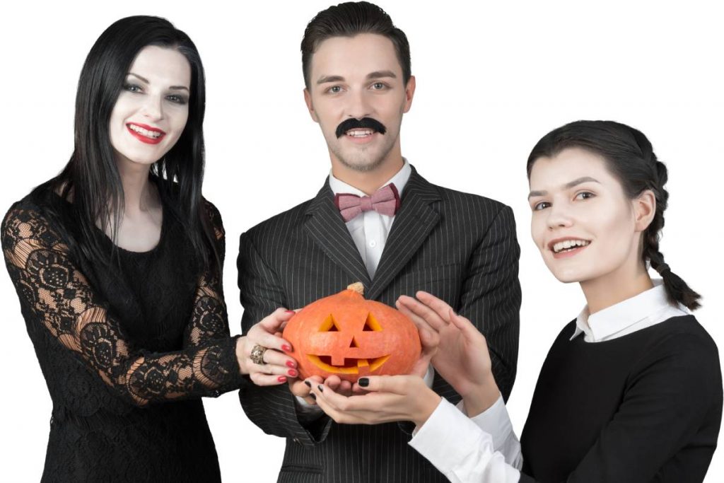 three people in halloween costumes posing with a pumpkin